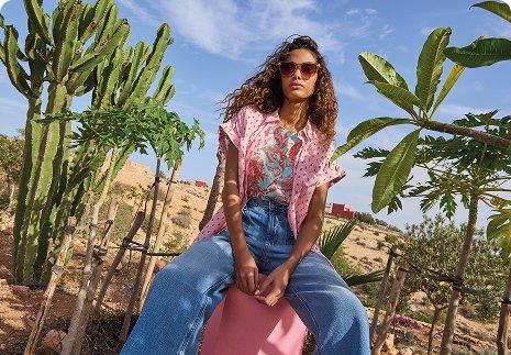 a woman sitting on a pink bucket in front of cactus plants